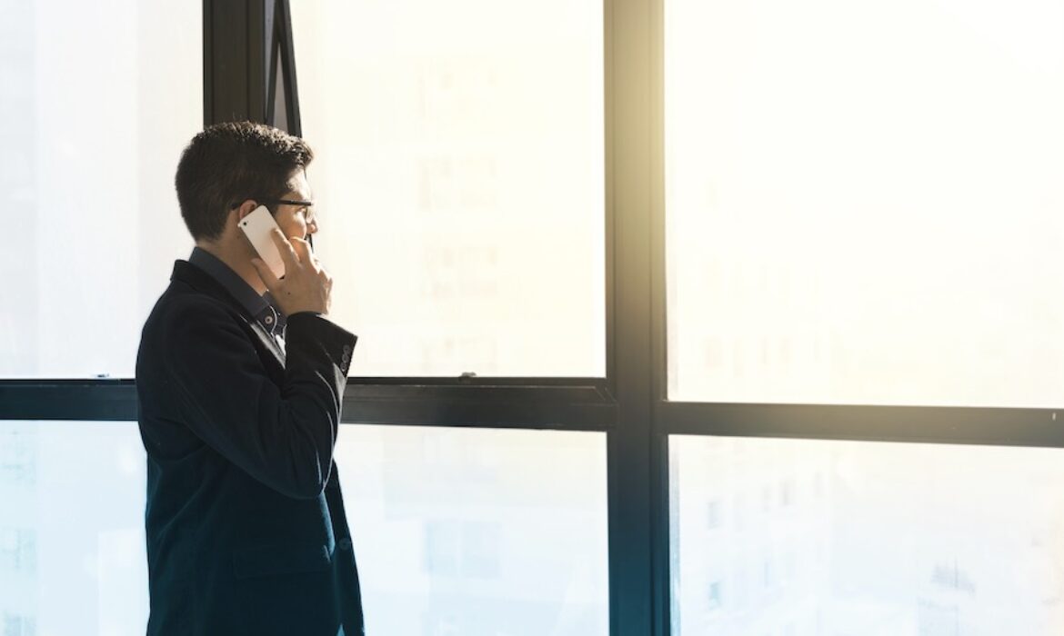 A man on the phone looking out of the window at a bright sunrise - the feeling of working for yourself